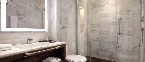 A modern bathroom with a marble vanity, a toilet, a glass-enclosed shower, and a large mirror.