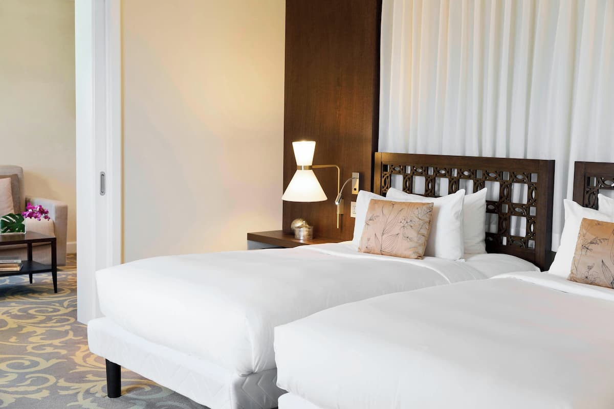 A hotel room with two beds, a nightstand with a lamp, a chair, and a decorative wall panel.