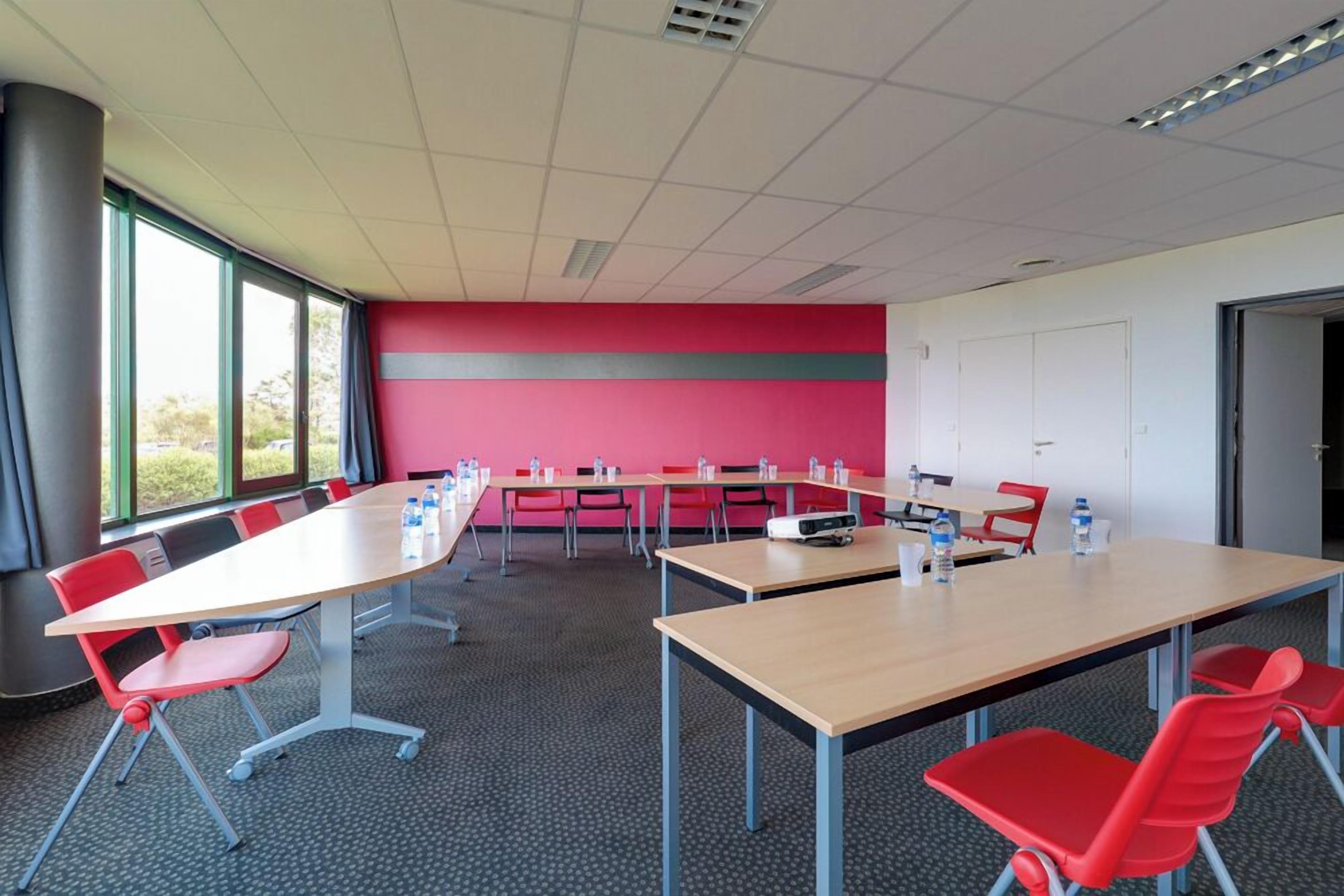 A conference room with a long table, red chairs, and a projector.