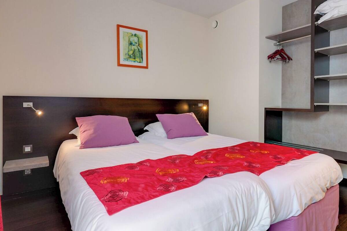 Una cama doble con colcha floral roja, dos almohadas moradas y un cabecero de madera.