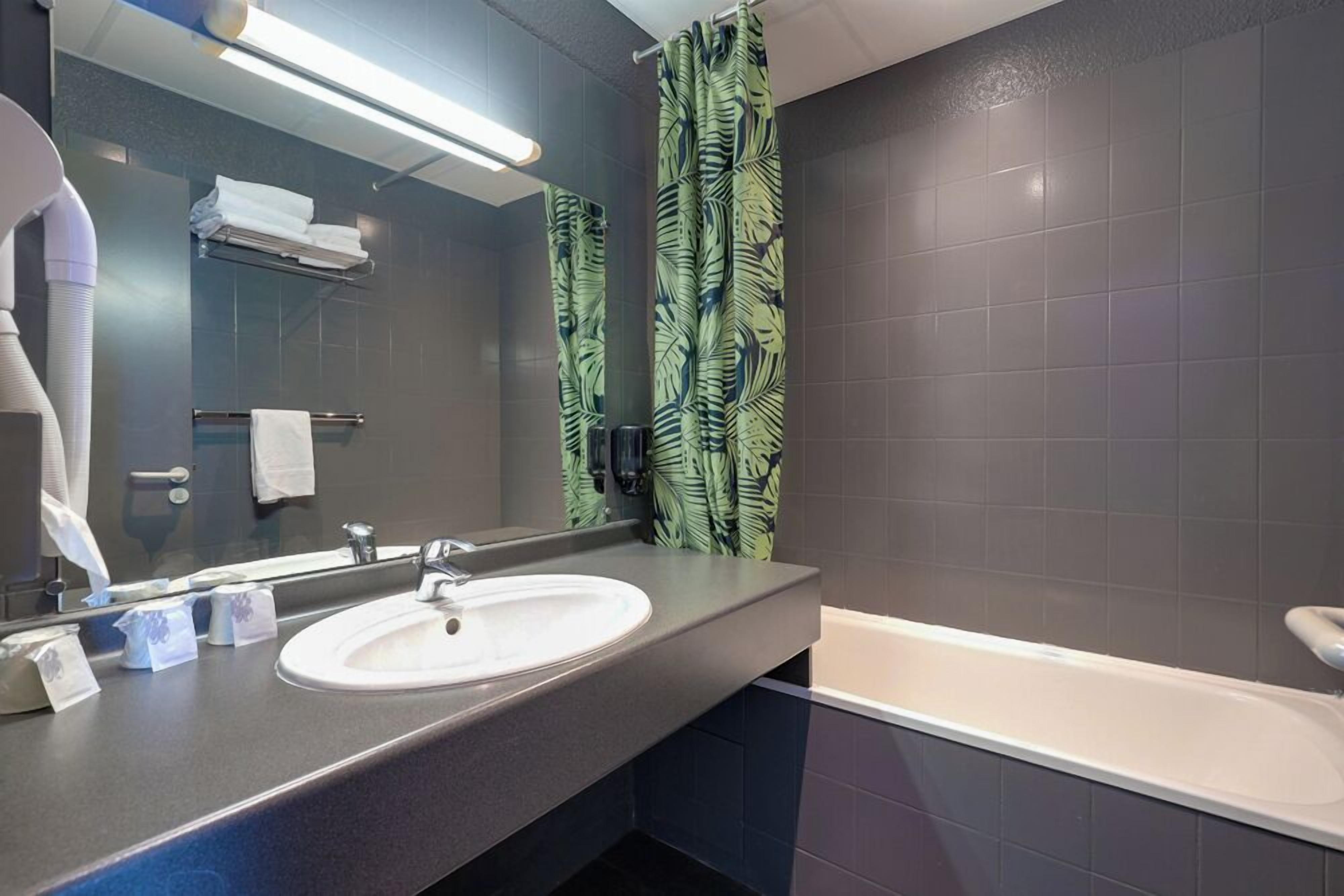 A modern bathroom with a large mirror, a white sink, a bathtub, and a shower curtain with a leaf pattern.