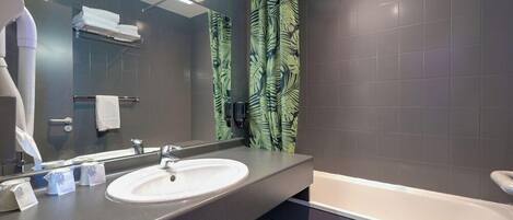 A modern bathroom with a large mirror, a white sink, a bathtub, and a shower curtain with a leaf pattern.