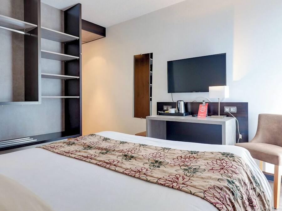 Ein Hotelzimmer mit Bett, Fernseher, Schreibtisch mit Lampe und Stuhl.