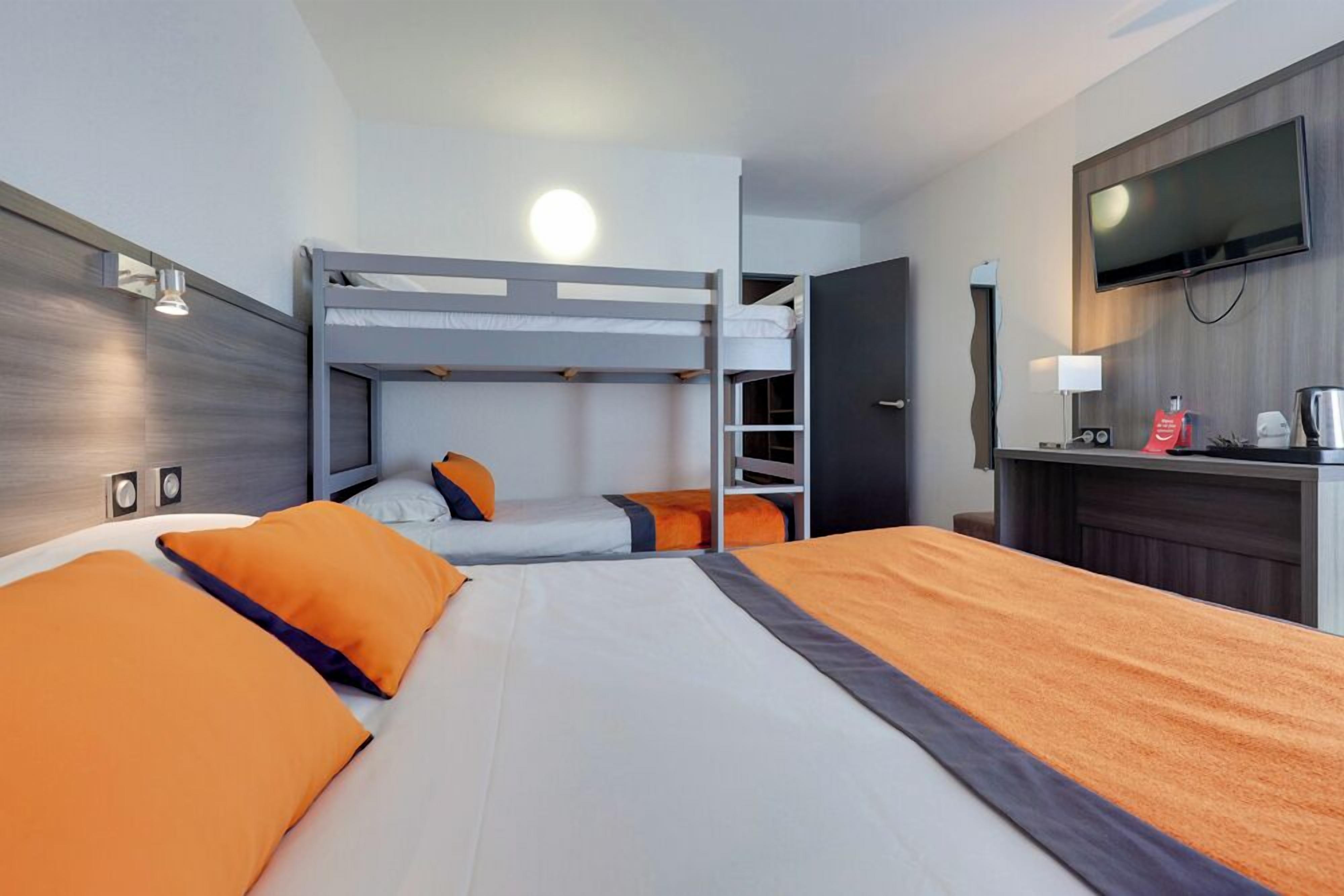 A hotel room with a bunk bed, a desk with a flat-screen TV, and a wall-mounted TV.