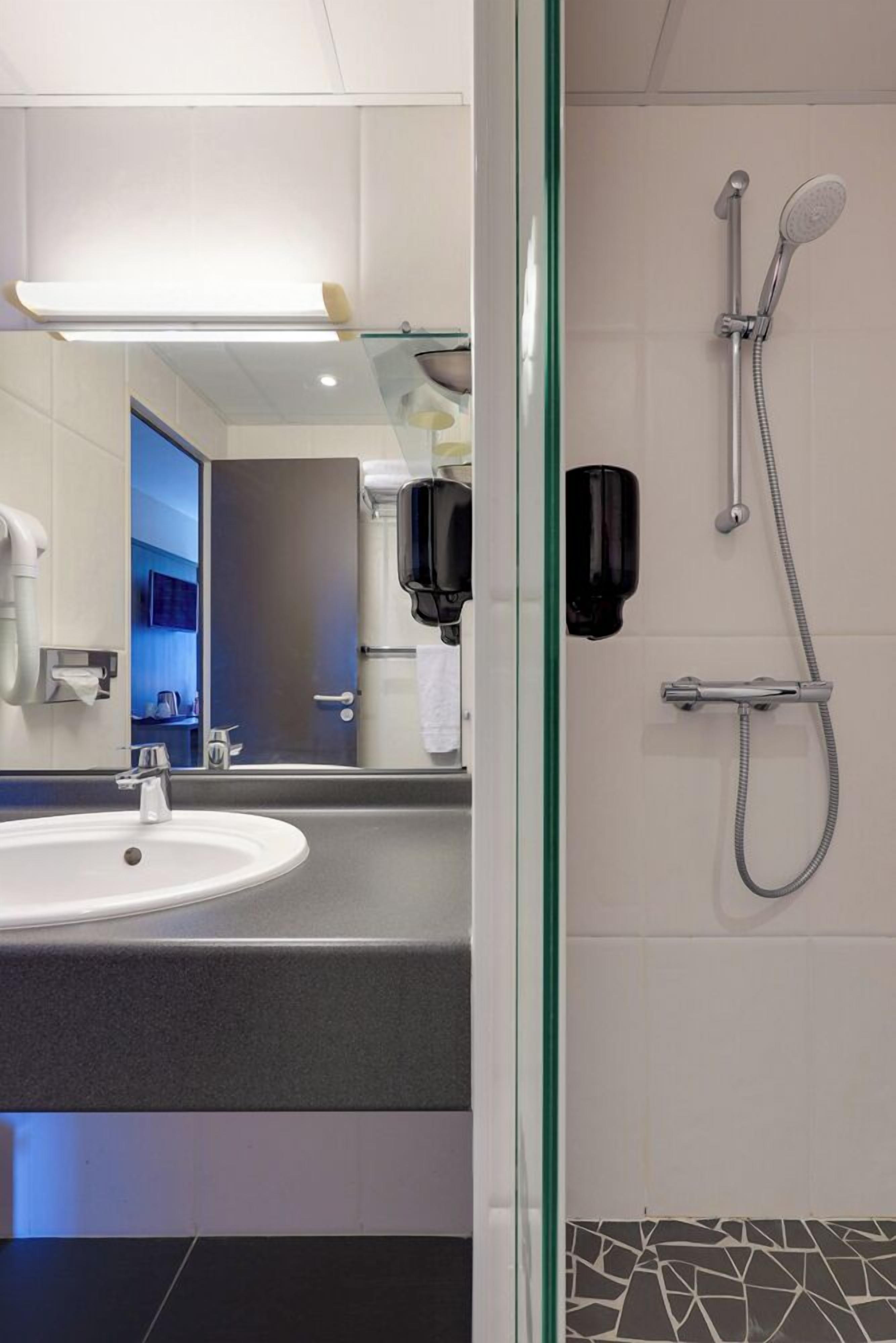 Un baño moderno con lavamanos, espejo y ducha.