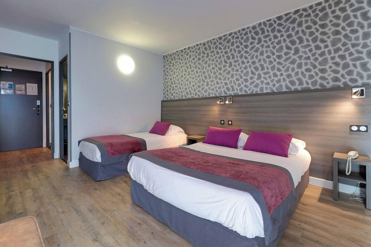Habitación de hotel con dos camas, un papel tapiz estampado con jirafas, suelo de madera y una mesita de noche con un teléfono.