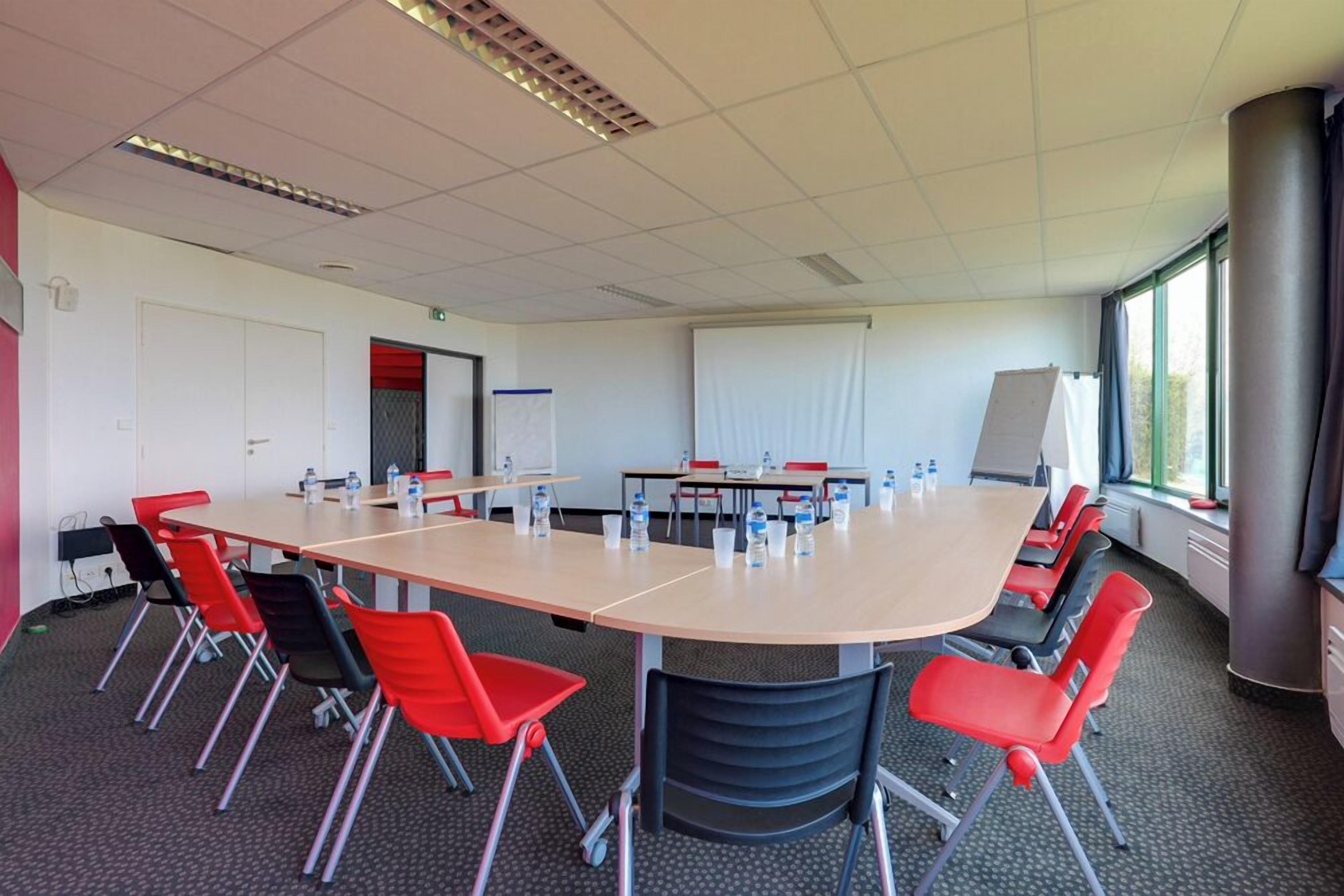 A conference room with a large table, chairs, water bottles, a whiteboard, and a projector screen.