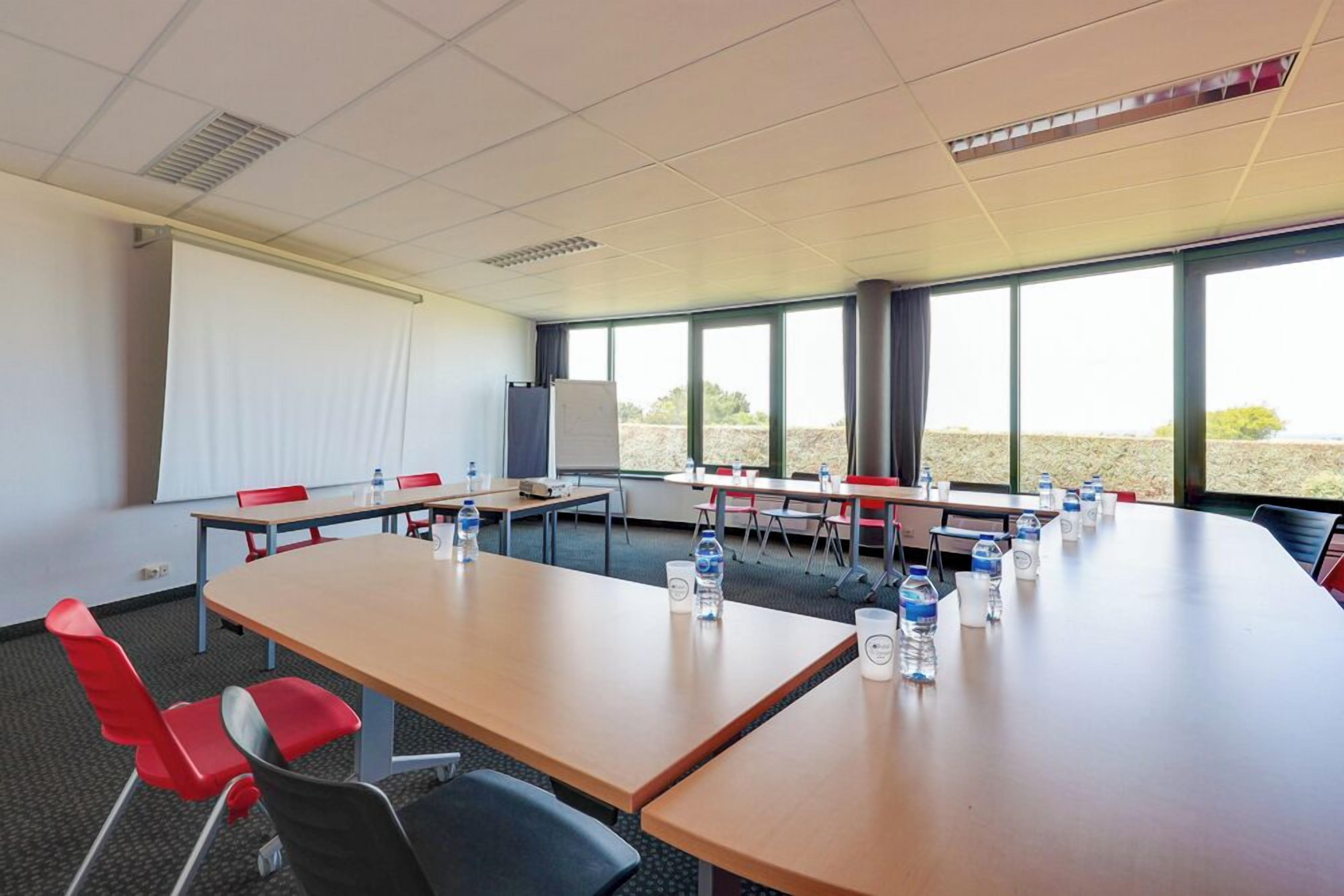 A conference room with a large table, red chairs, water bottles, and a projector screen.