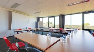 A conference room with a large table, red chairs, water bottles, and a projector screen.