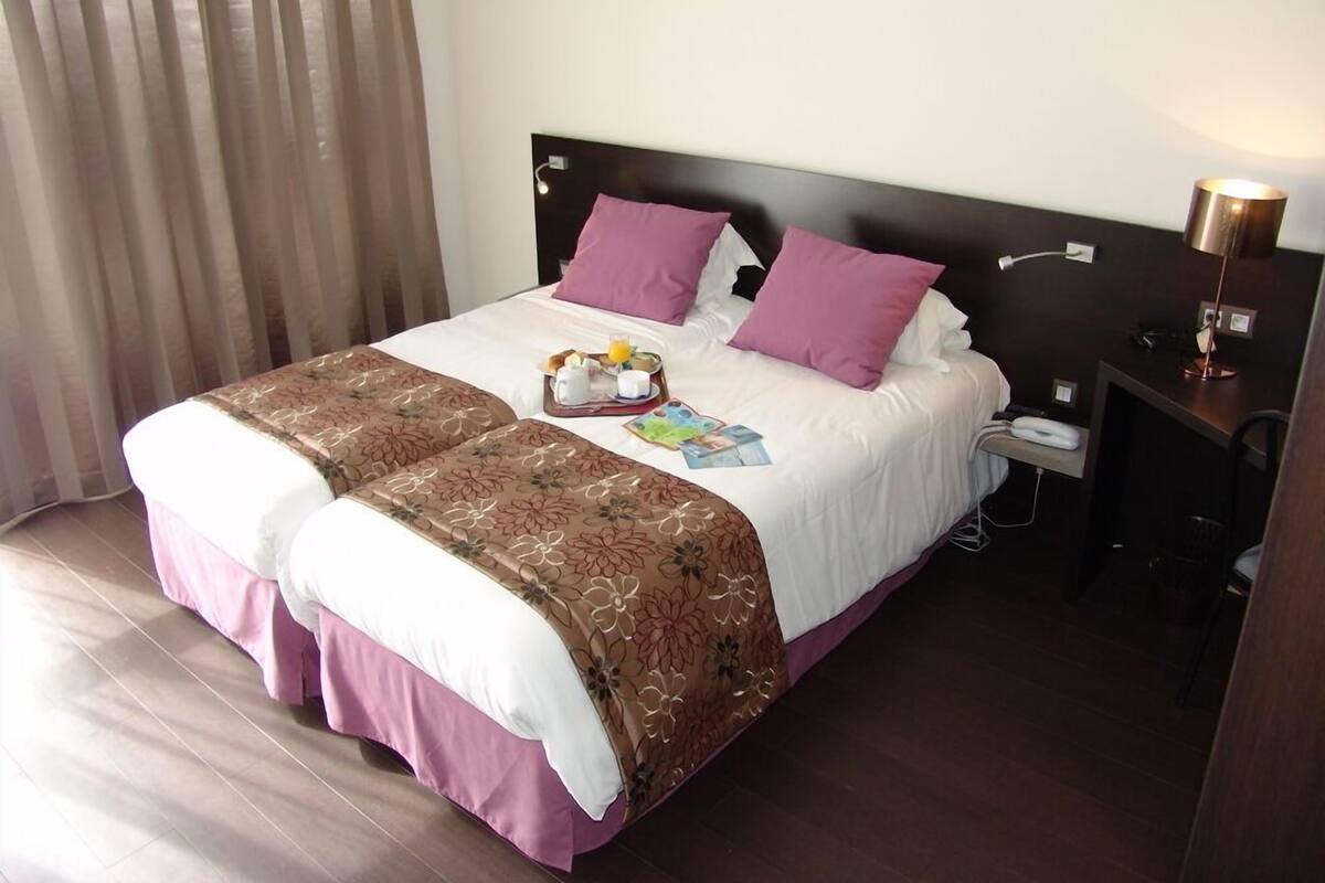 Una habitación de hotel con una cama, una mesita de noche con lámpara y una ventana con cortinas.