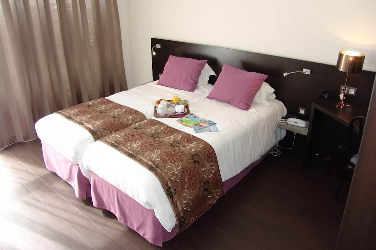 Une chambre d’hôtel avec un lit, une table de chevet avec une lampe et une fenêtre avec des rideaux.