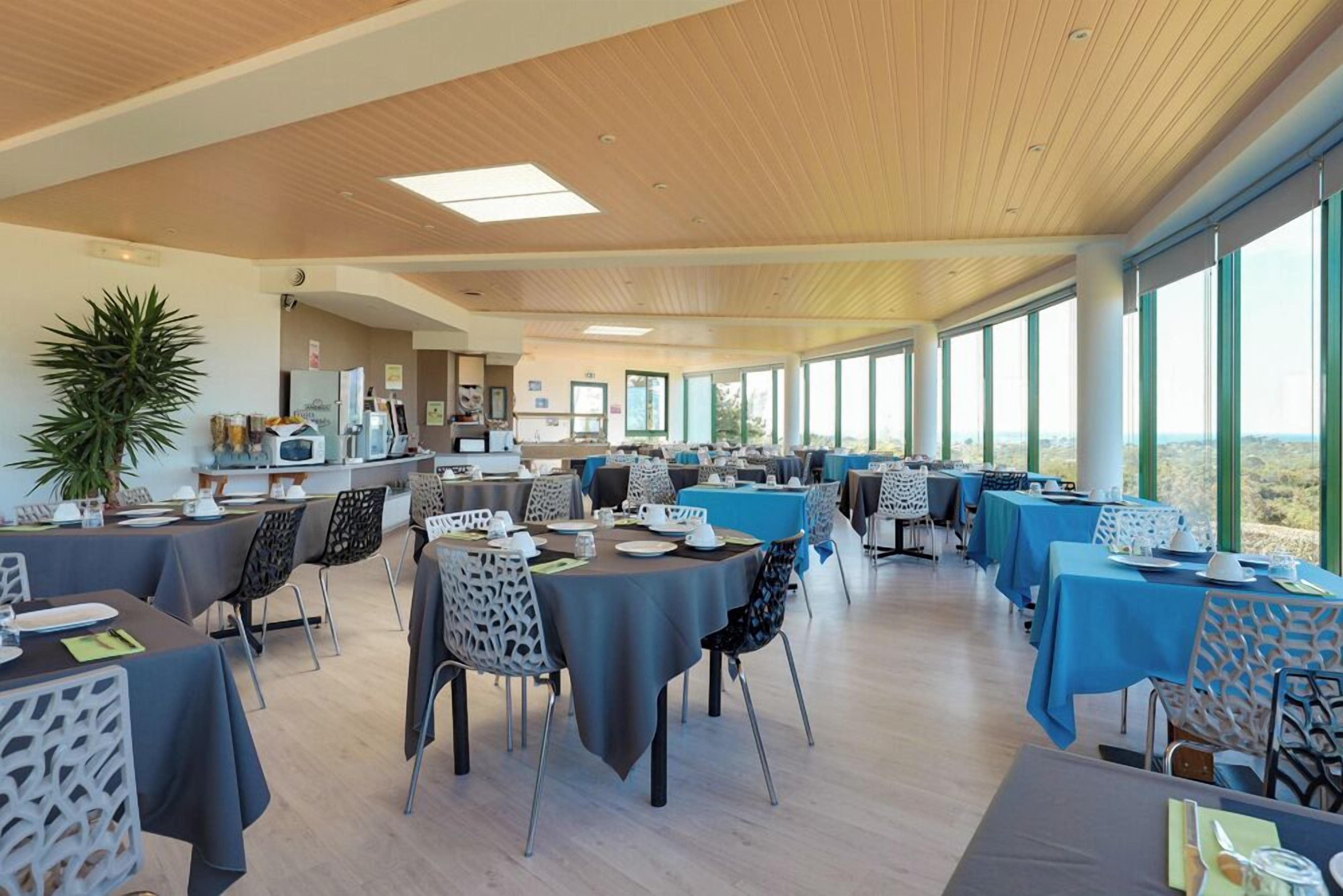 A spacious dining area with high ceilings and large windows, featuring modern furniture and a view of the landscape.