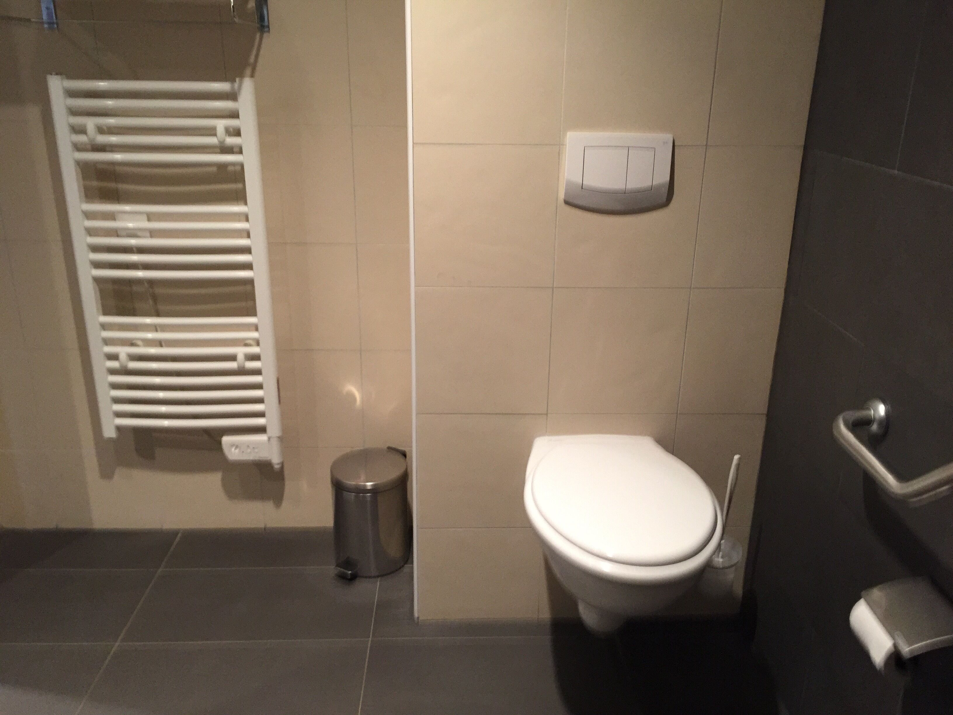 A bathroom with a toilet, a trash bin, a towel rack, and a toilet paper holder.