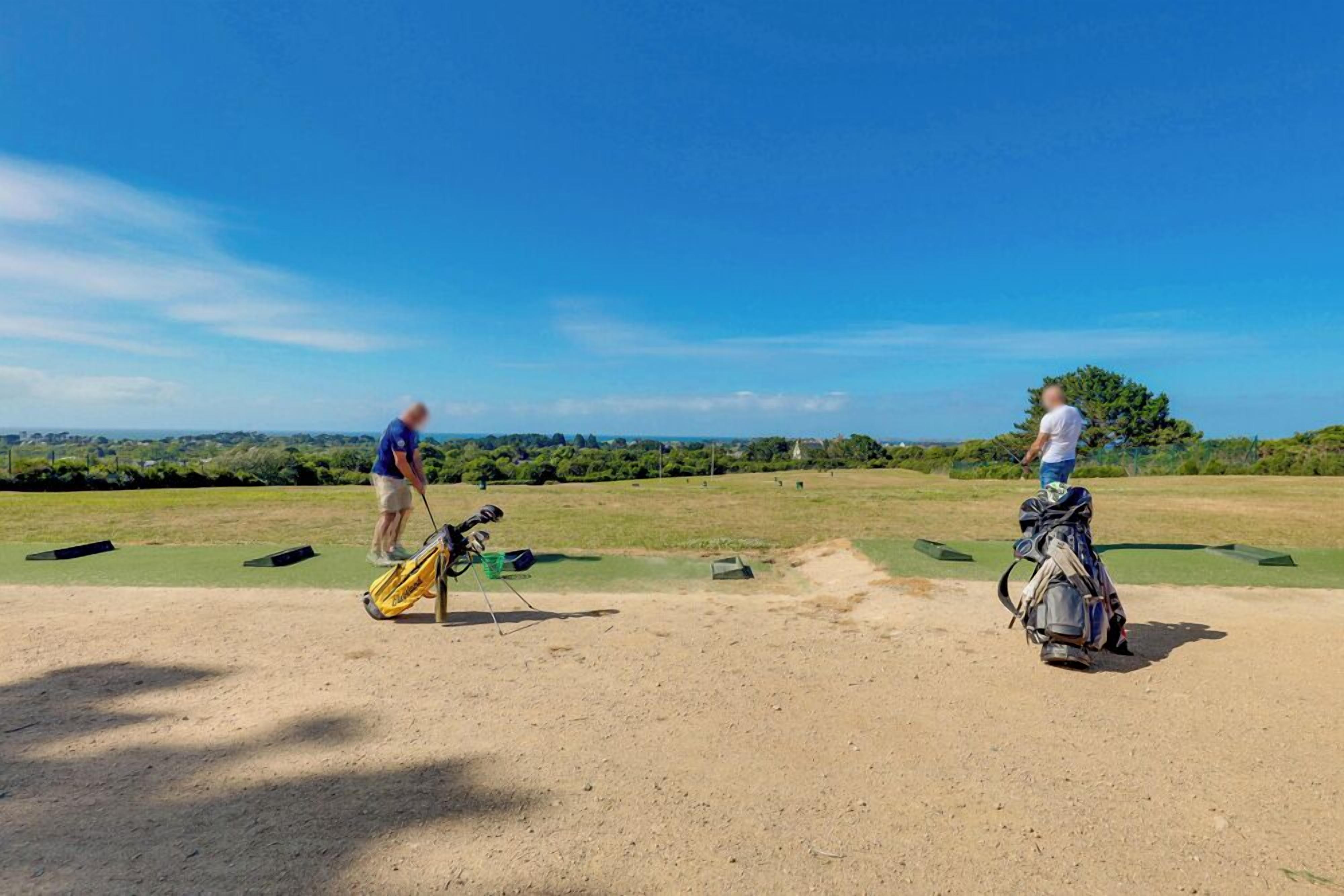 En golfbane med to personer der forbereder sig på at spille, en golftaske og en klar blå himmel.
