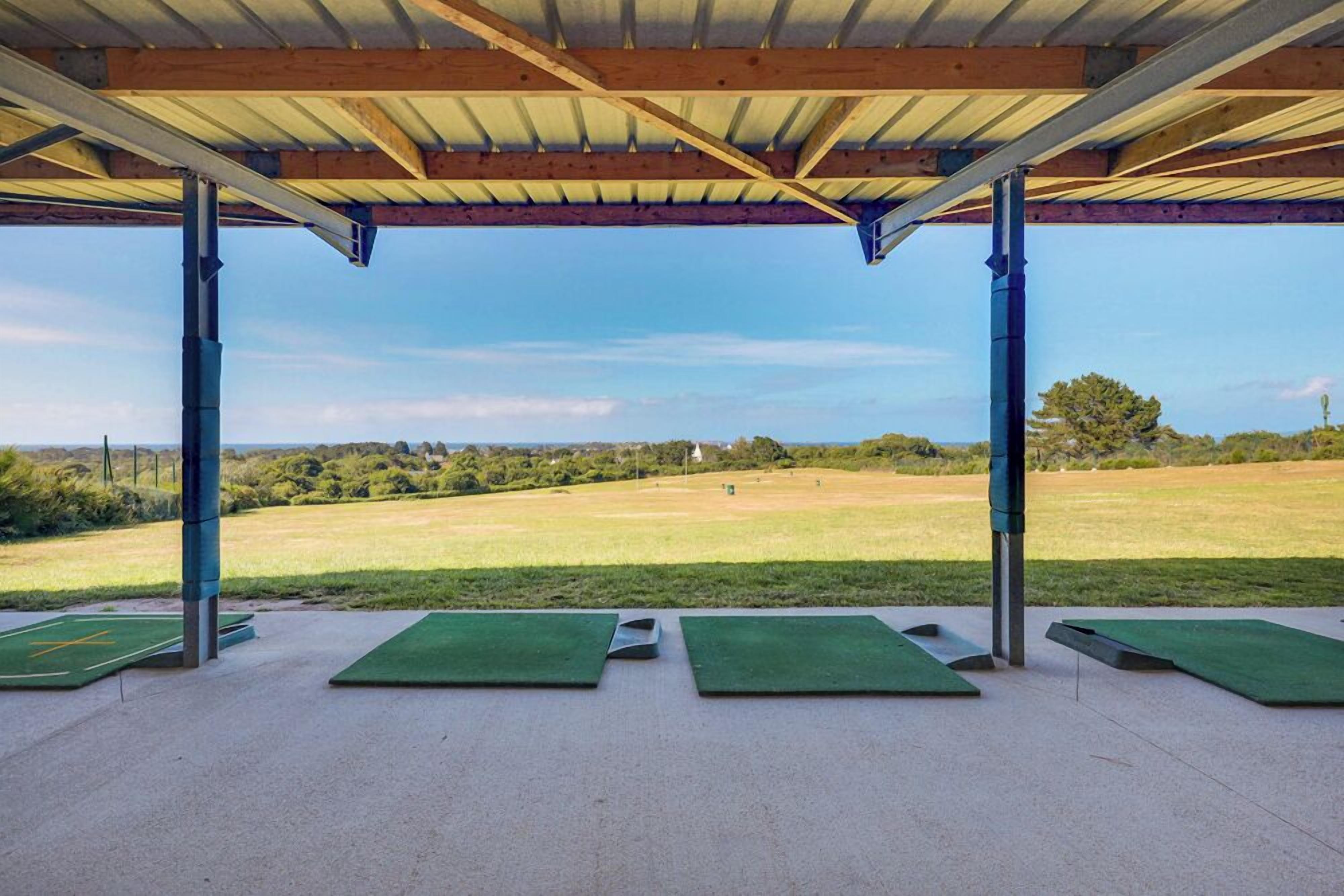 A covered outdoor area with green mats, metal poles, and a view of a grassy field.
