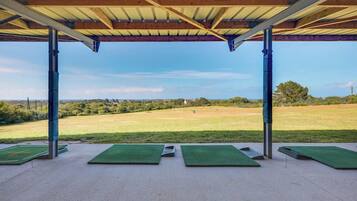 A covered outdoor area with green mats, metal poles, and a view of a grassy field.
