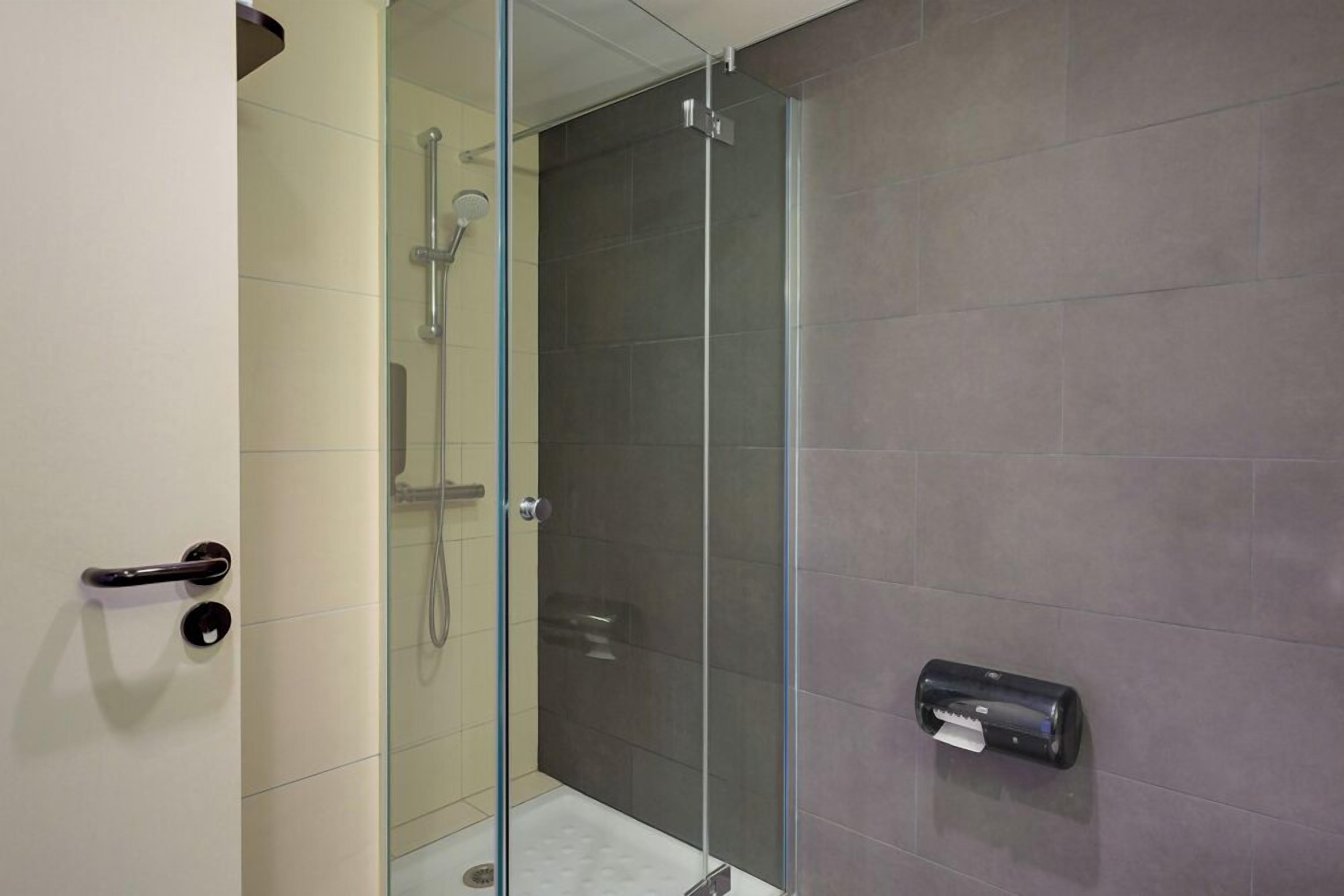 A modern bathroom with a glass shower enclosure, a towel dispenser, and a door with a handle.