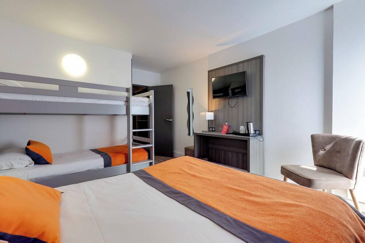 Una habitación de hotel con literas, un escritorio con televisor de pantalla plana, una silla y una chimenea.