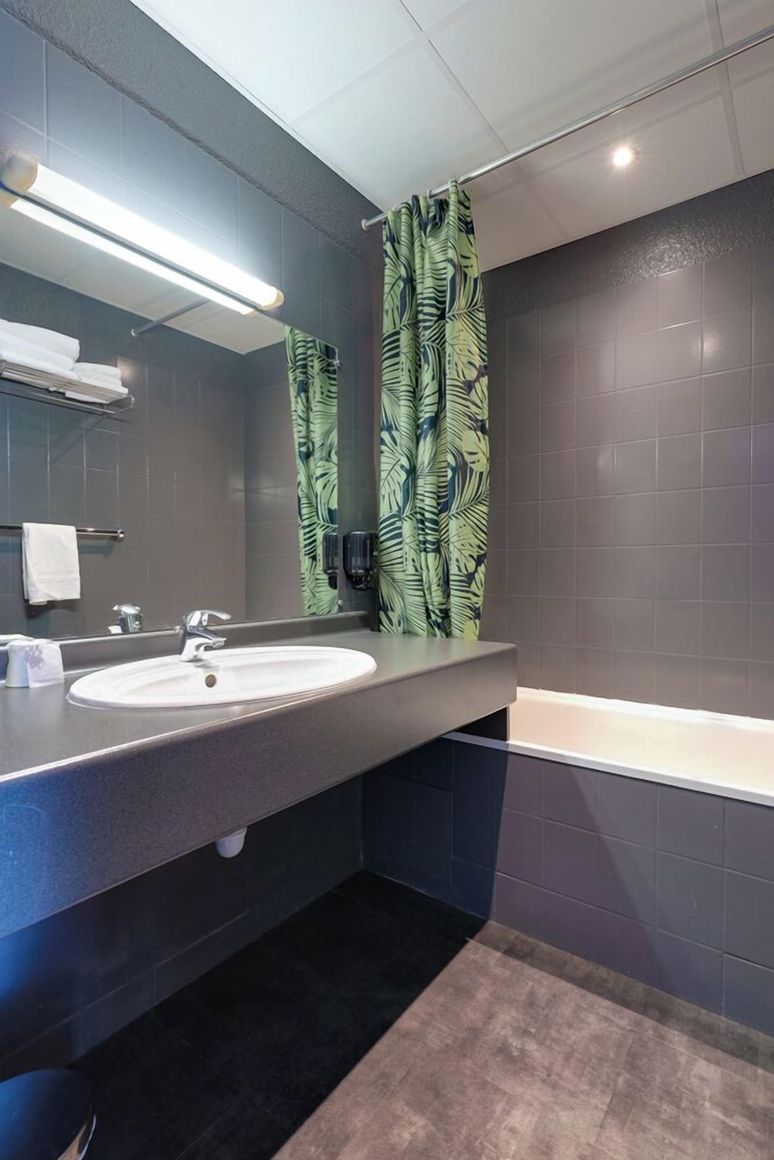 A modern bathroom with a large sink, mirror, and a shower curtain with a leaf pattern.
