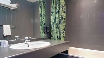 A modern bathroom with a large sink, mirror, and a shower curtain with a leaf pattern.