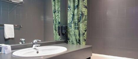 A modern bathroom with a large sink, mirror, and a shower curtain with a leaf pattern.