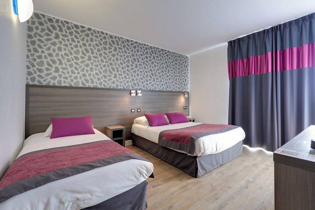 Habitación de hotel con dos camas, cabecero con textura, mesita de noche y escritorio.