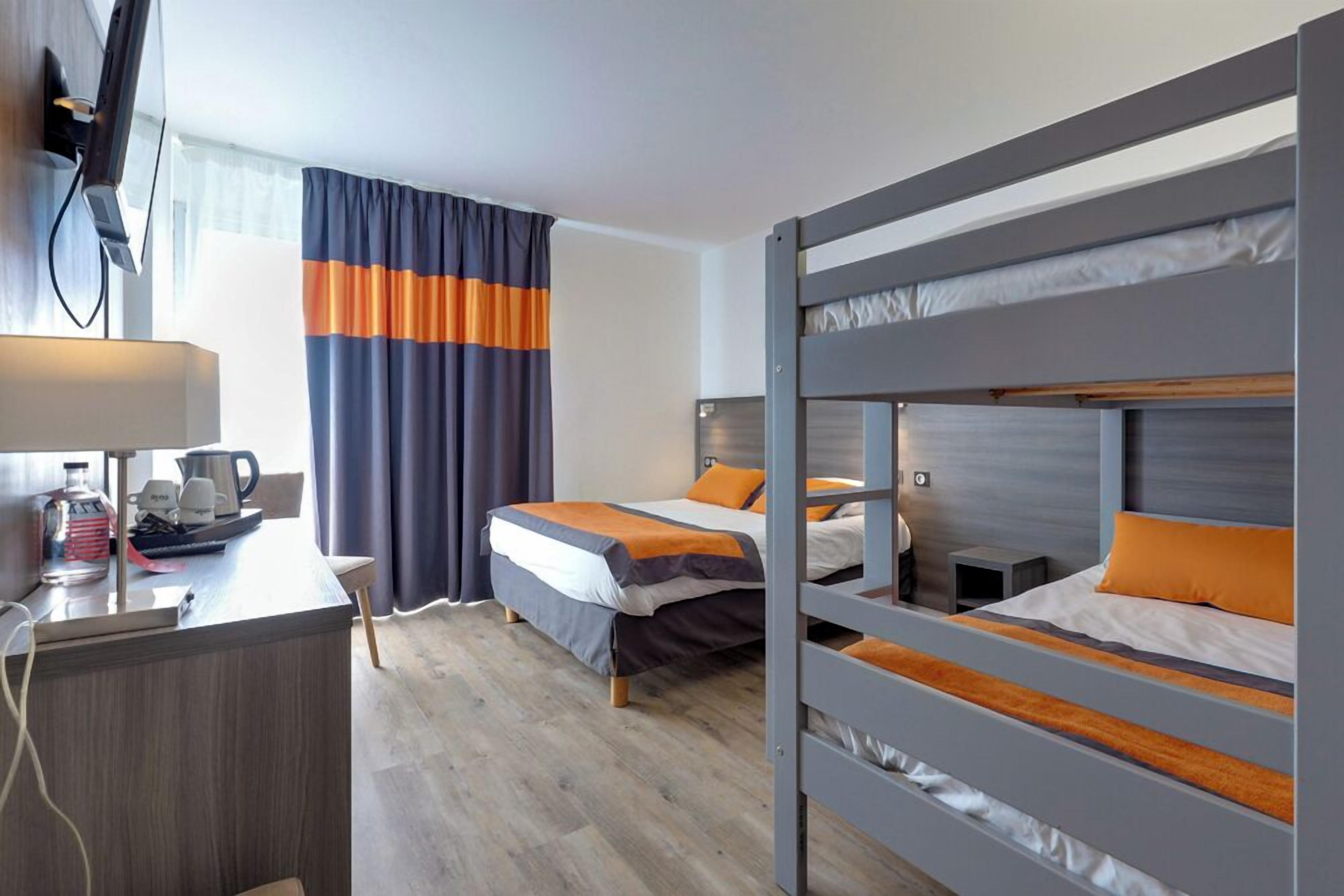 Habitación de hotel con dos camas, un escritorio con lámpara, televisor y ventana con cortinas.