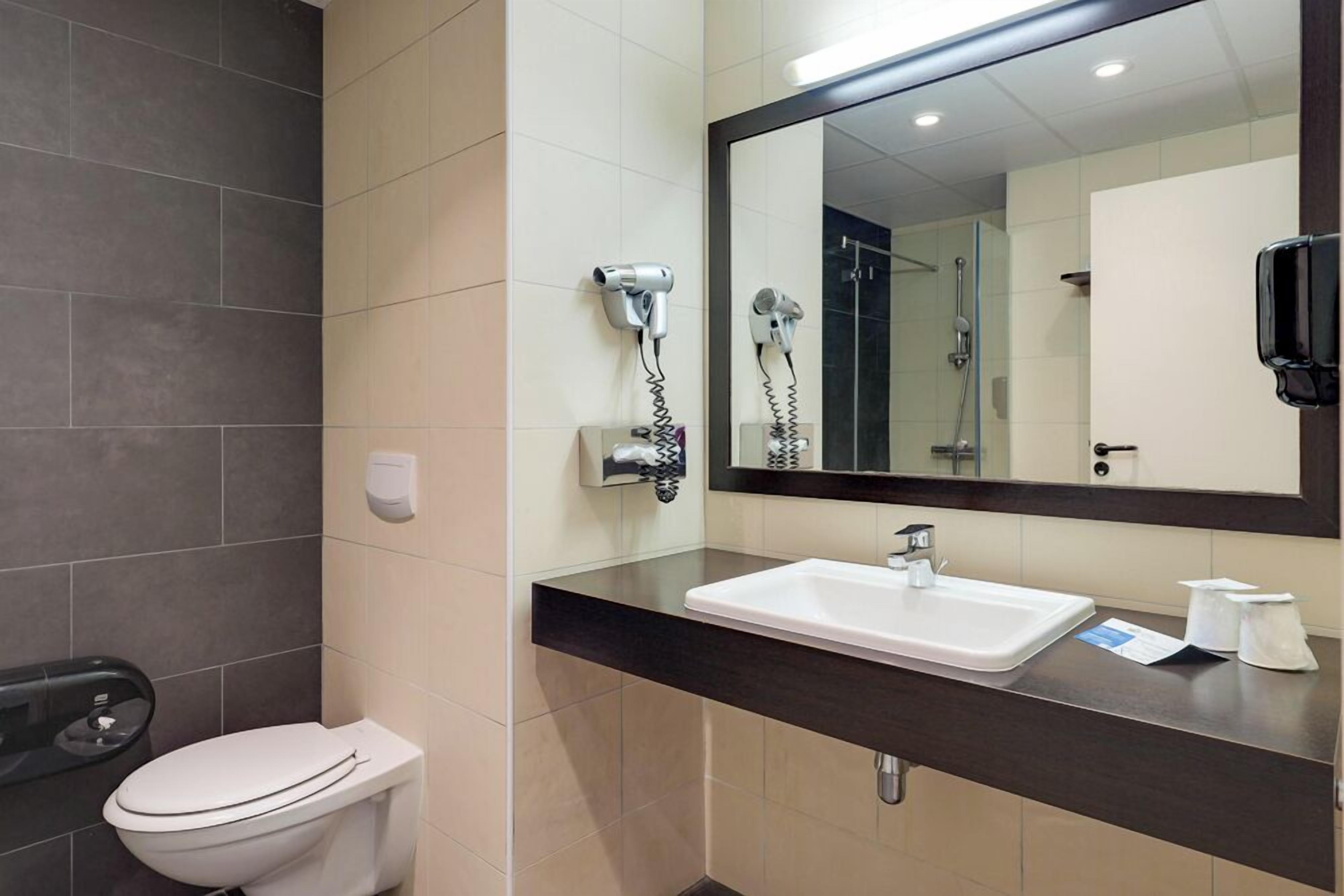 A bathroom with a toilet, a sink, a mirror, and a hairdryer mounted on the wall.