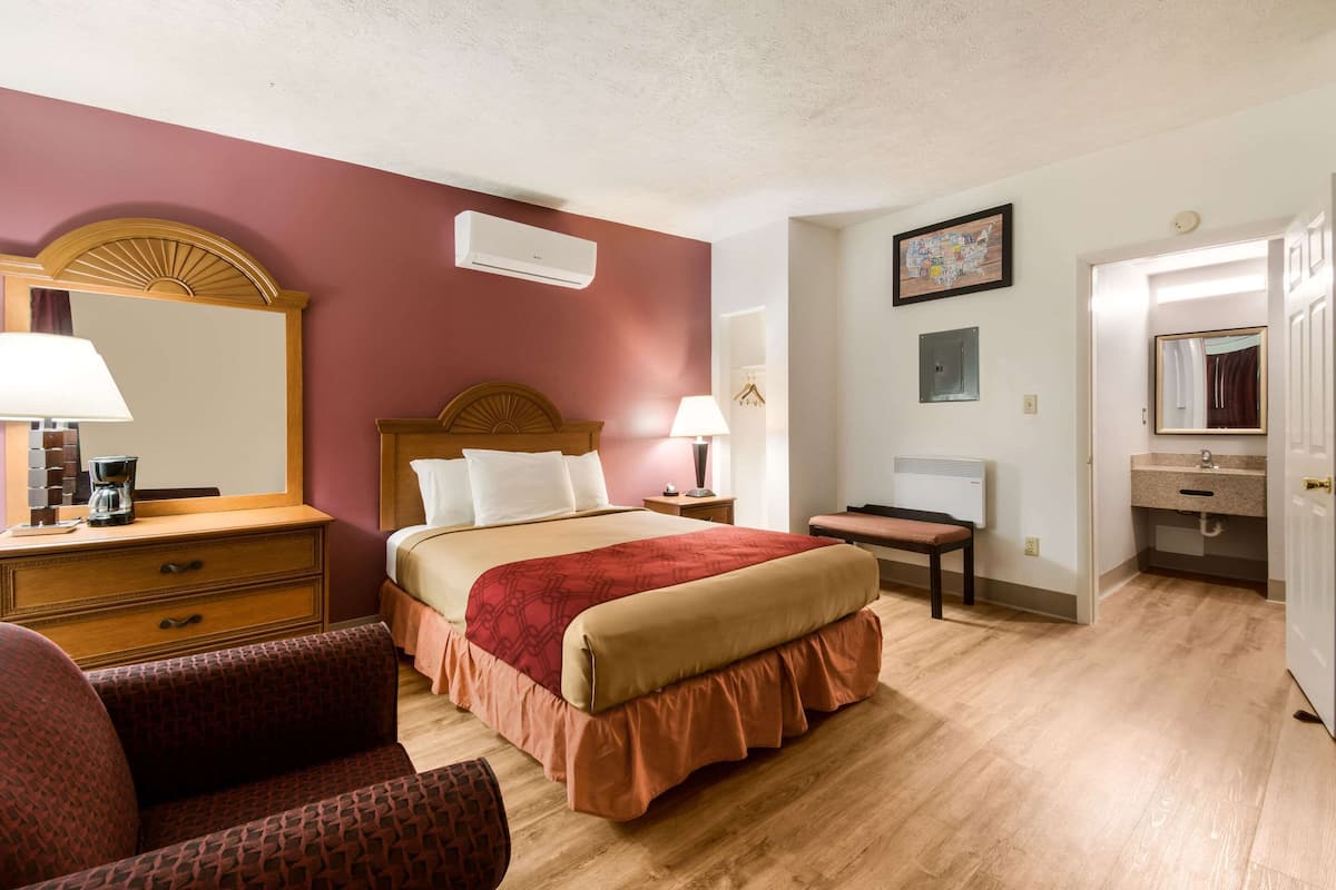 A hotel room with a bed, a desk, a chair, a dresser, and a bathroom.
