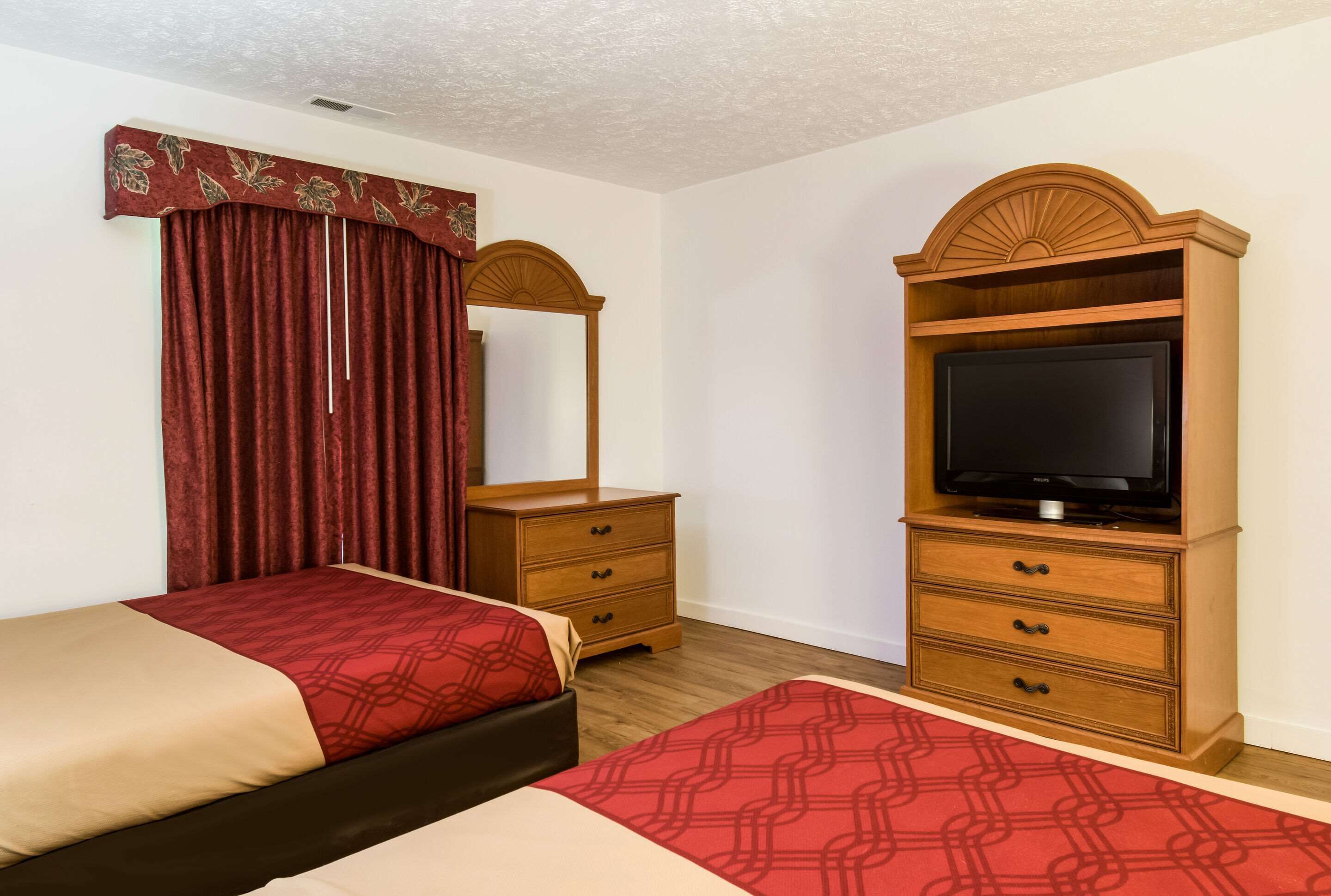 Una habitación de hotel con dos camas, un aparador de madera con televisor y un espejo sobre el aparador.