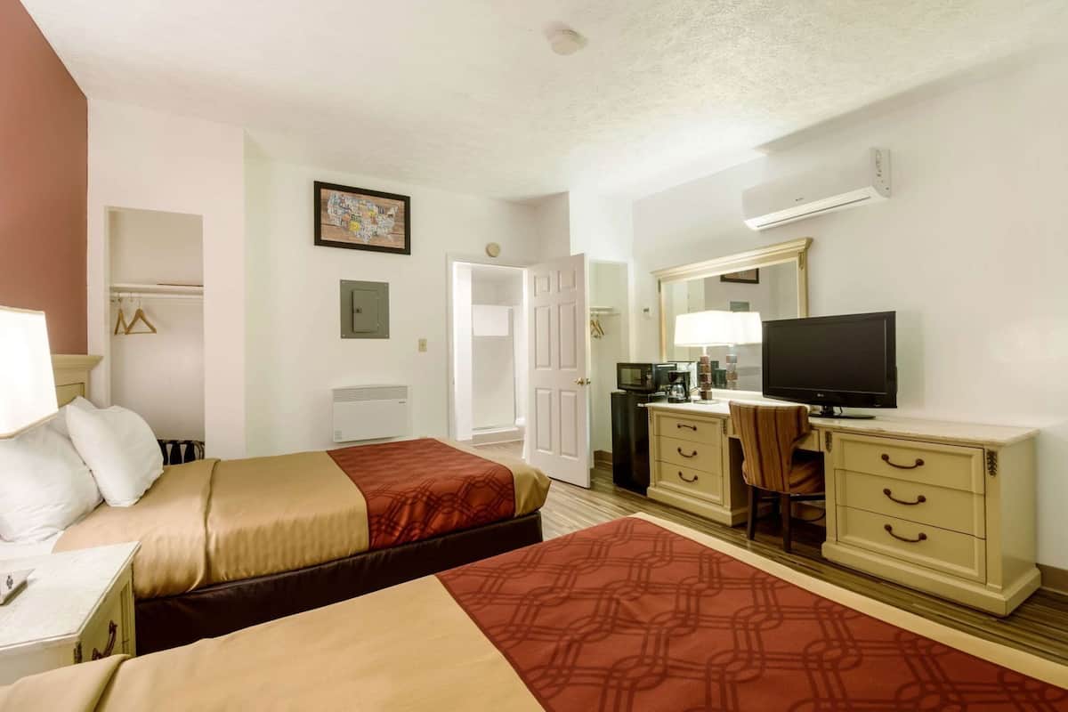 A hotel room with two beds, a desk with a television, a dresser, and a microwave.