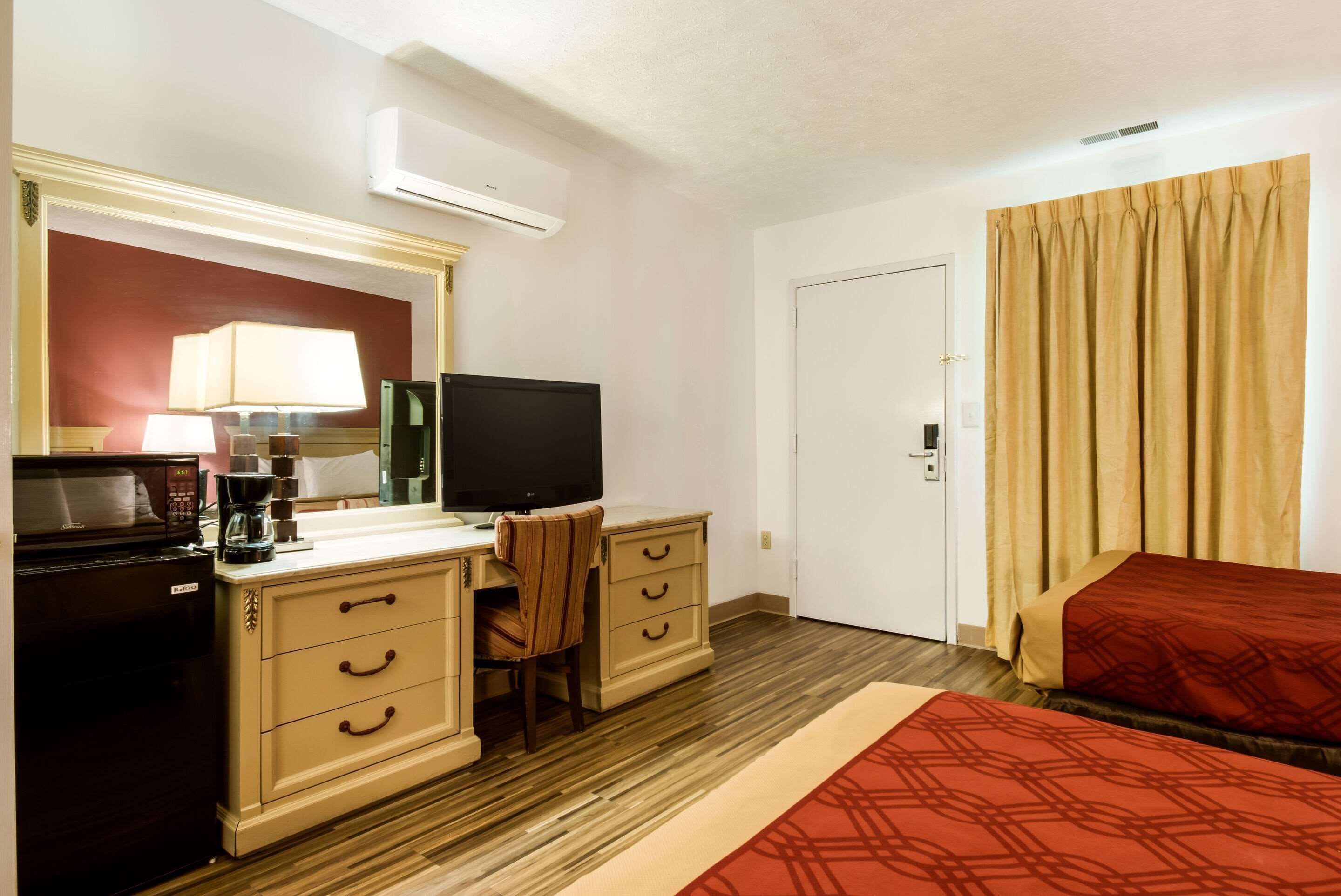 Habitación de hotel con kitchenette, televisión, escritorio con silla, cama y ventana con cortinas.