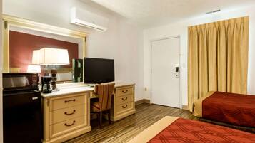 Habitación de hotel con kitchenette, televisión, escritorio con silla, cama y ventana con cortinas.