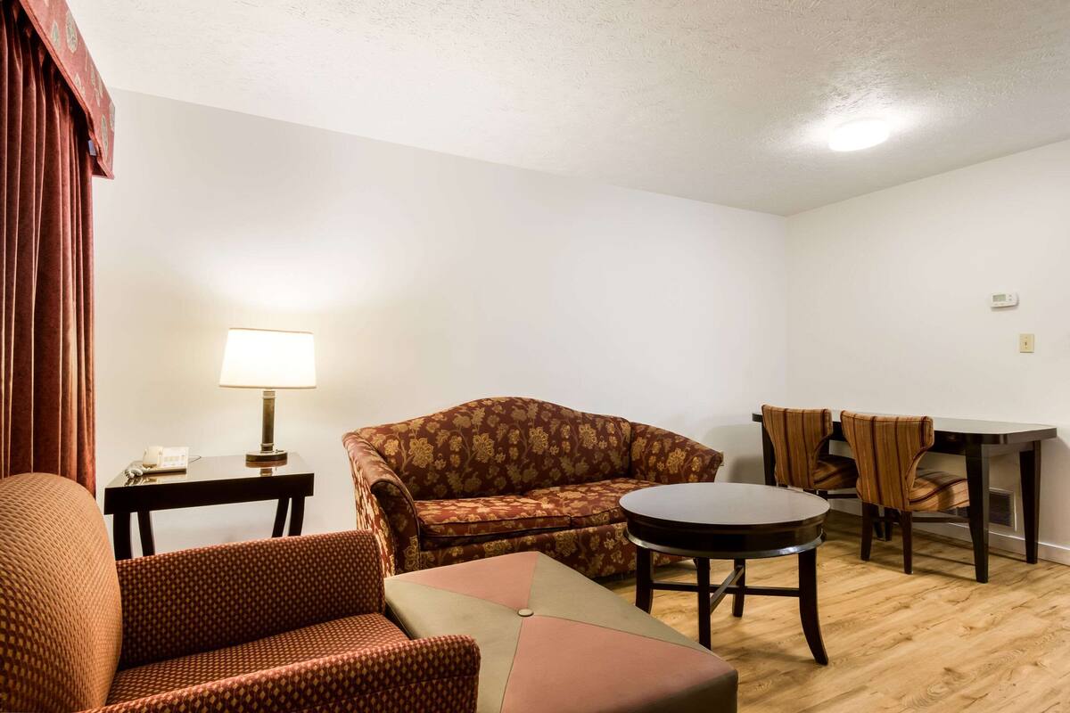 A living room with a sofa, armchair, and a small round table. There is a lamp on a side table, and a dining table with chairs.