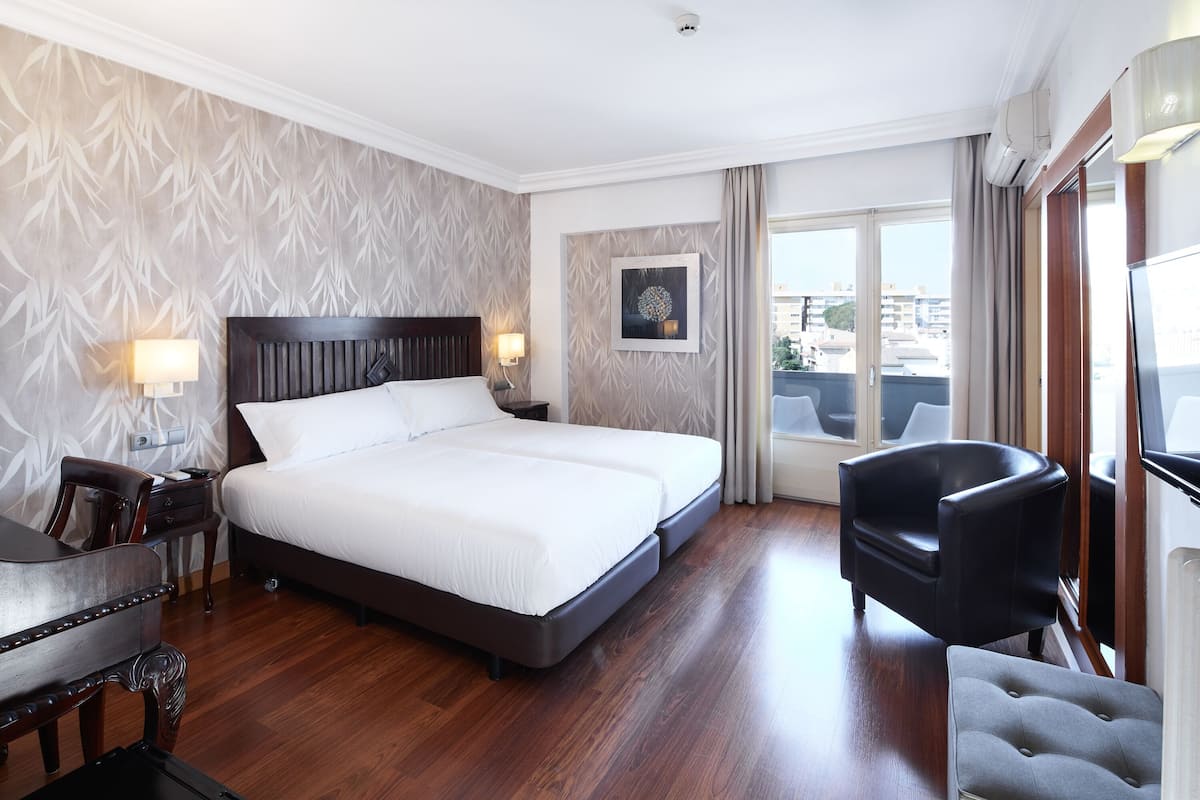 Ein Hotelzimmer mit einem großen Bett, einem Schreibtisch, einem Stuhl und Blick auf die Stadt durch das Fenster.