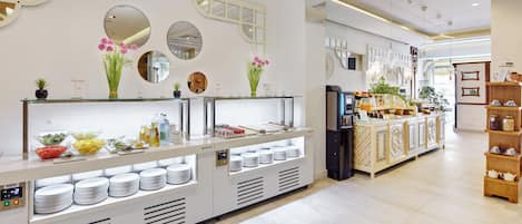 Un café moderno con mostrador de autoservicio, espejos y diversas opciones de comida y bebida.
