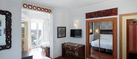 Habitación de hotel con cama, escritorio, silla, televisor y puerta corrediza que da a un balcón.