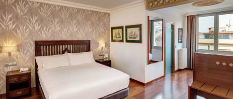 Habitación de hotel con una cama grande, cabecera de madera, lámparas de noche, mesita de noche, un banco de madera y vistas por la ventana.