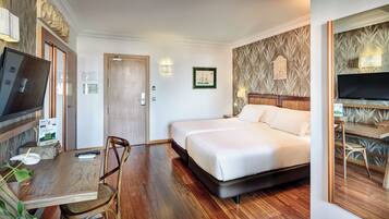 A hotel room with a bed, a desk with a chair, a television, and a wall-mounted lamp.
