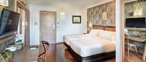 Habitación de hotel con cama, escritorio, silla, televisor y lámpara de pared.