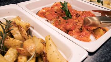 A white rectangular serving dish with roasted potatoes and a tomato-based sauce, garnished with a sprig of rosemary.
