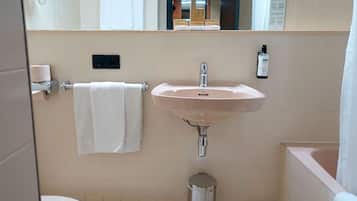 Un baño con lavamanos, espejo, toallero y cubo de basura.