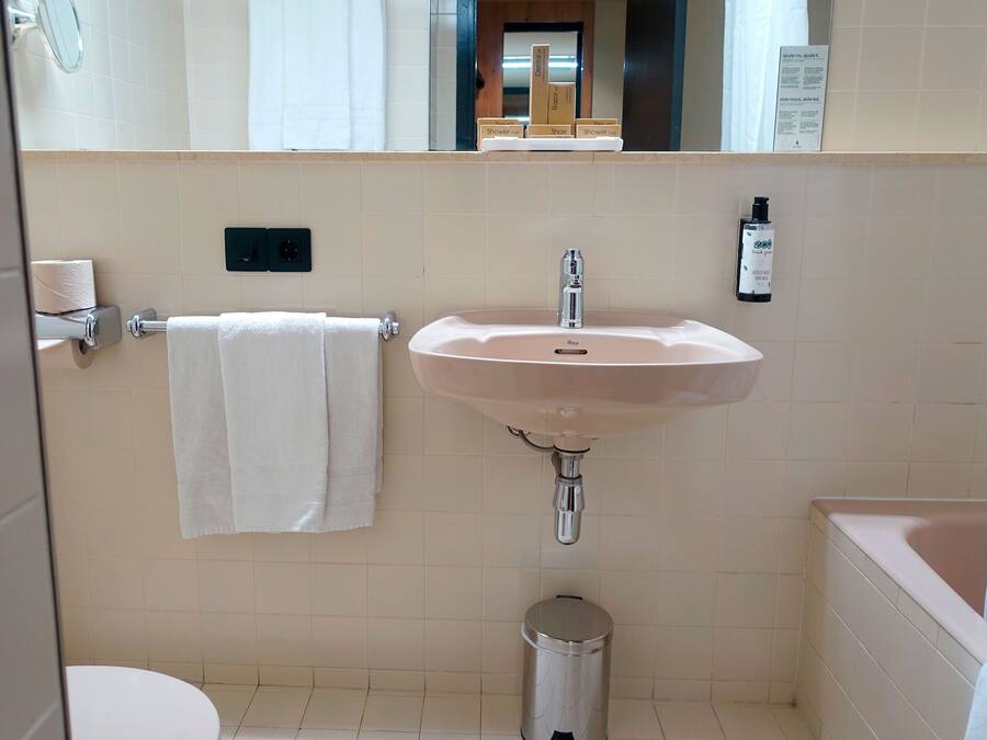 Un baño con lavamanos, espejo, toallero y cubo de basura.