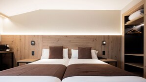 Habitación de hotel con dos camas, cabecero de madera, mesitas de noche y un armario empotrado con estantes.