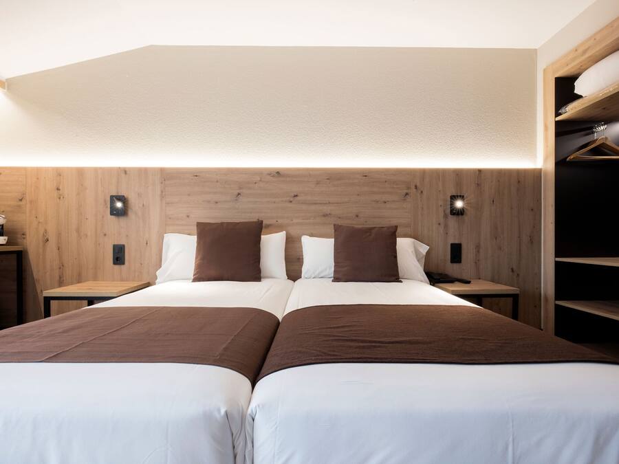 A hotel room with two beds, wooden headboard, bedside tables, and a built-in closet with shelves.