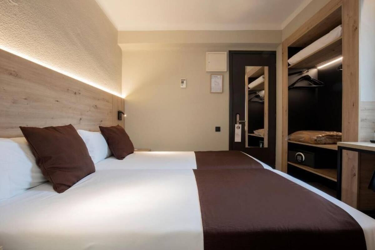 Hotellihuone, jossa on kaksi sänkyä, puinen pääty, erillinen vaatehuone ja yöpöytä.