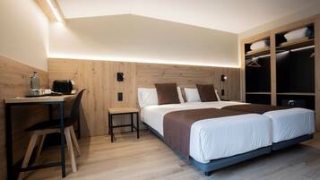 A modern hotel room with a wooden desk, a bed with a brown headboard, and a walk-in closet with hanging space.