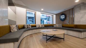 Un intérieur moderne avec un espace salon aux lignes courbes, une table basse ronde et un panneau indiquant la présence d’un restaurant.