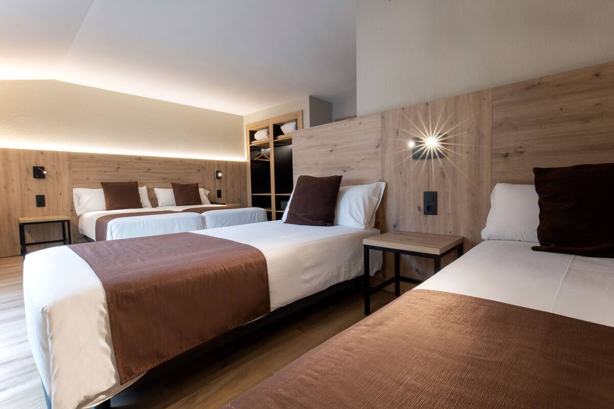 Moderni hotellihuone, jossa on kaksi sänkyä, puinen pääty, yöpöytä ja sisäänrakennettu vaatekaappi.