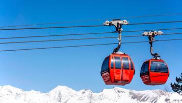 Two red cable cars suspended by a cable system against a clear blue sky, with snow-covered mountains in the background.
